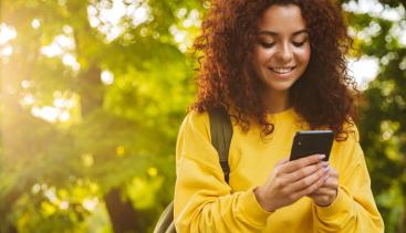 Woman happily using a phone in a green park